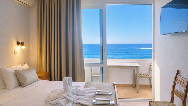 A hotel room with a bed, a table, and a view of the ocean. - Klinakis Beach Hotel (Chania)