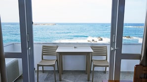 A balcony with a table and two chairs, overlooking a rocky coastline and the sea. - Klinakis Beach Hotel (Chania)