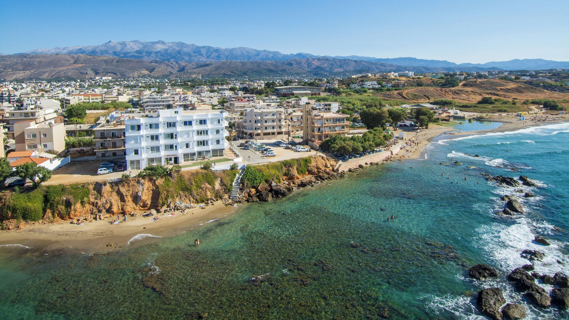Ein Hotel an der Küste mit mehreren Etagen, einer Strandlage und klarem, blauem Wasser.
