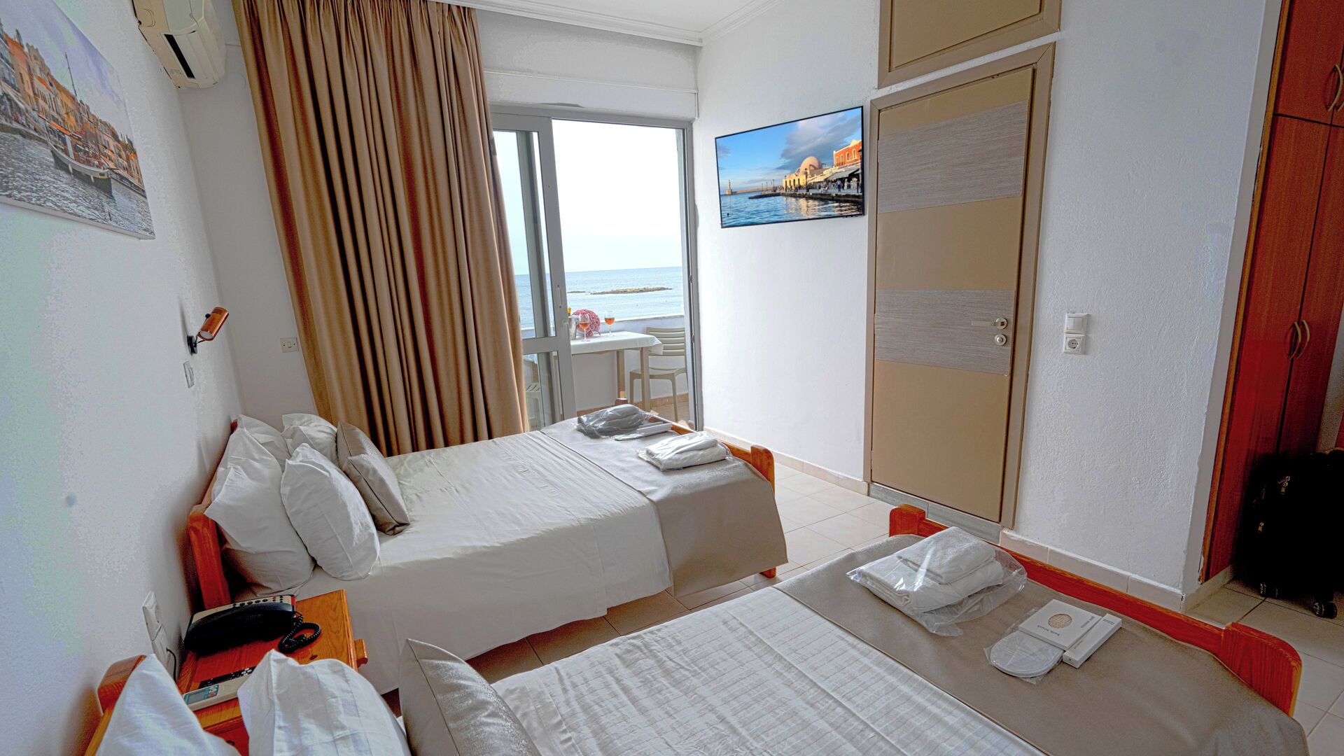 A hotel room with two beds, a TV, a window with a view of the sea, and a door with a mirror.
