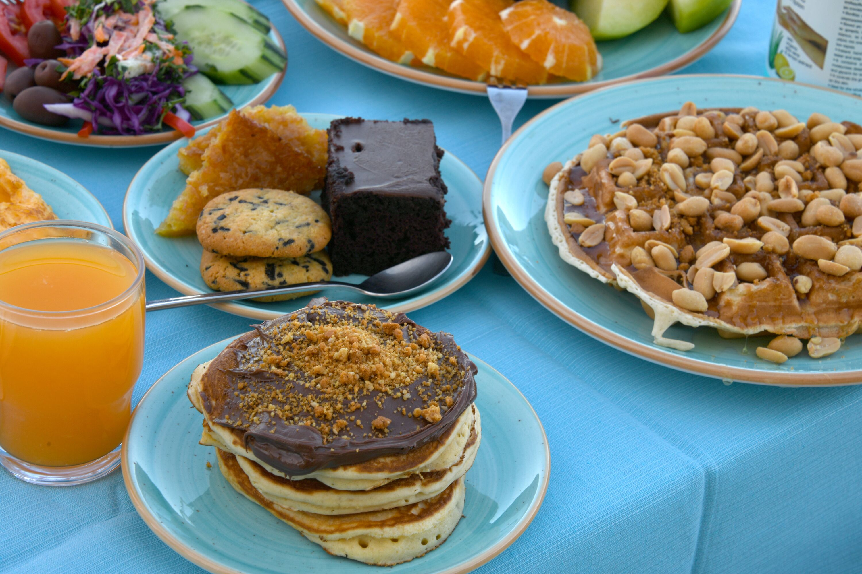 A table with various food items including pancakes, a chocolate cake, and a plate of nuts.