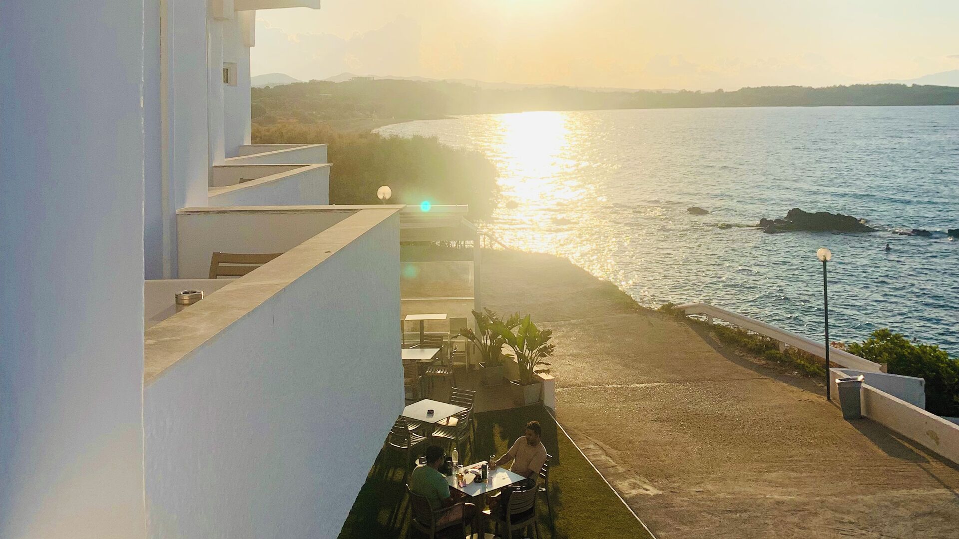 Blick auf das Meer vom Balkon mit Tisch und Stühlen, überblickt ein ruhiges Meer und einen Sonnenuntergang.