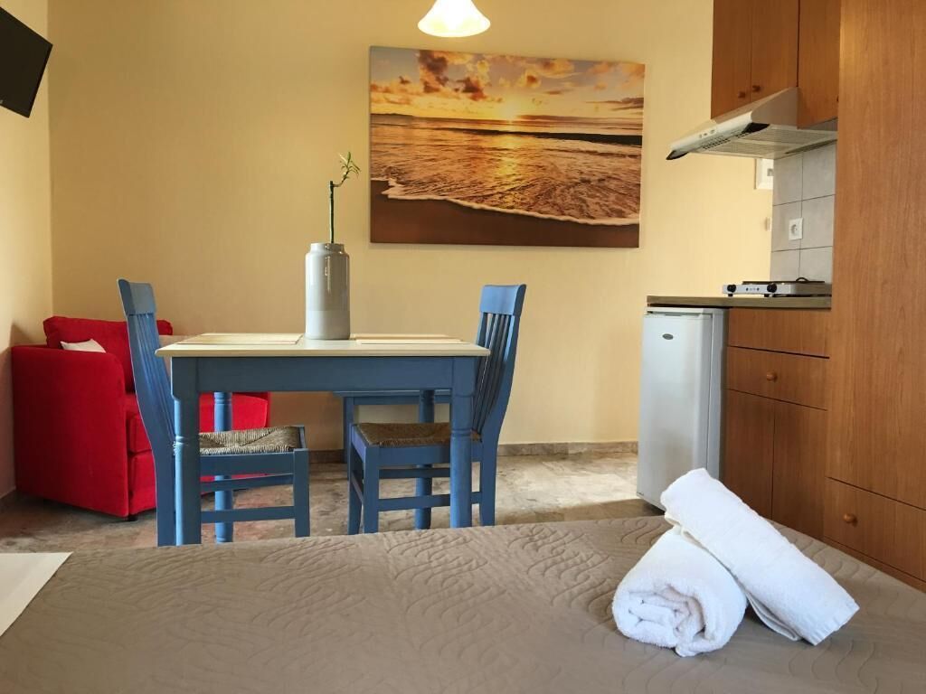 A room with a bed, a table with chairs, a small kitchenette, and a painting of a sunset over the ocean.