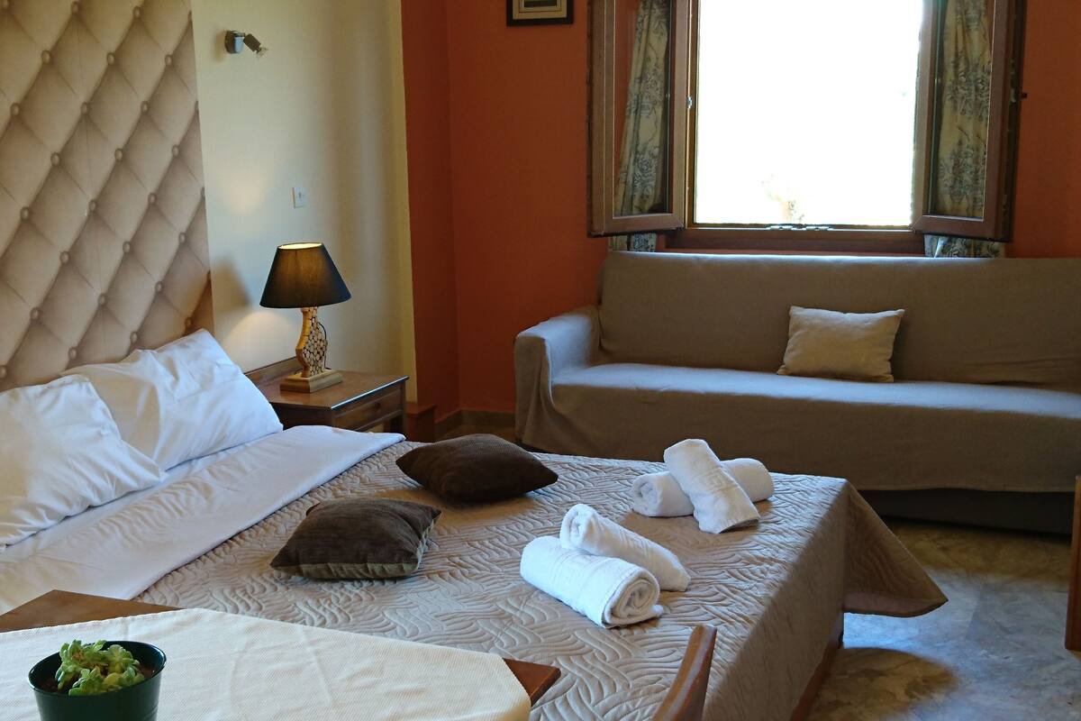 A hotel room with a bed, a sofa, a lamp, and a window.