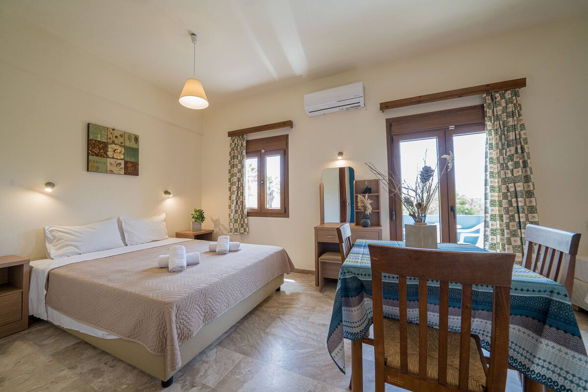 A bedroom with a bed, bedside tables, a desk, a chair, a mirror, and a window with curtains.