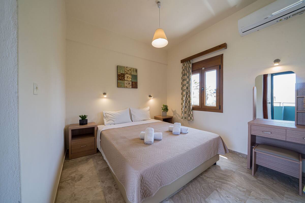 A bedroom with a bed, bedside tables, a dresser, a hanging light, and an air conditioning unit.
