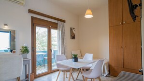 A modern room with a dining table, chairs, a wooden cabinet, and a sliding glass door leading to an outdoor area. - Frank Apartments (Malevizi)