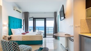 A modern hotel room with a large bed, a seating area, a TV, and a view of the sea. - Rethymno Hills Apartments (Rethymno)