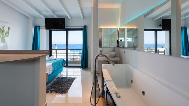 A modern hotel room with a balcony, a large mirror, a bathtub, and a view of the sea. - Rethymno Hills Apartments (Rethymno)
