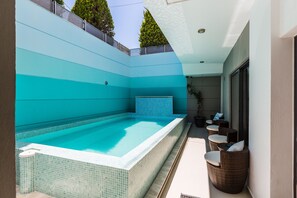 A swimming pool with a tiled edge, surrounded by a light-colored wall and a small seating area with wicker chairs and cushions. - Rethymno Hills Apartments (Rethymno)