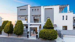 A modern two-story residential building with a balcony on the upper floor, a covered entrance, and three potted evergreen trees in front. - Rethymno Hills Apartments (Rethymno)