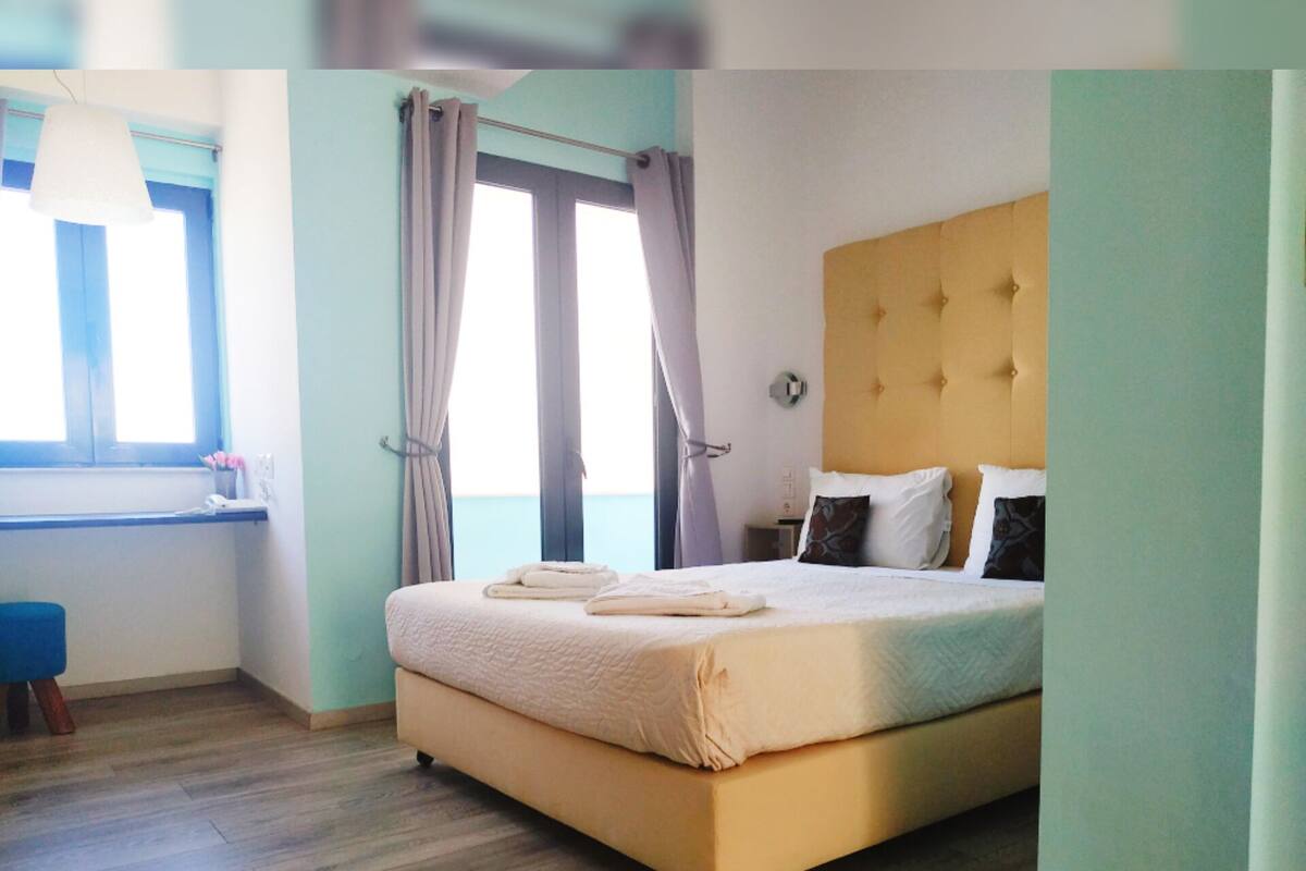 A bedroom with a bed, a desk, and a window with curtains.