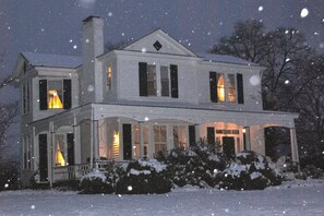 Uma casa de dois andares com entrada central, várias janelas e chaminé. Neve cai lá fora.