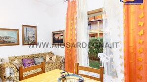 A room with a dining table, chairs, a decorative bowl, a sofa with patterned cushions, and a window with curtains.