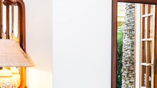 A room with a wooden bed frame, a bedside lamp, and a window with a view of greenery outside.