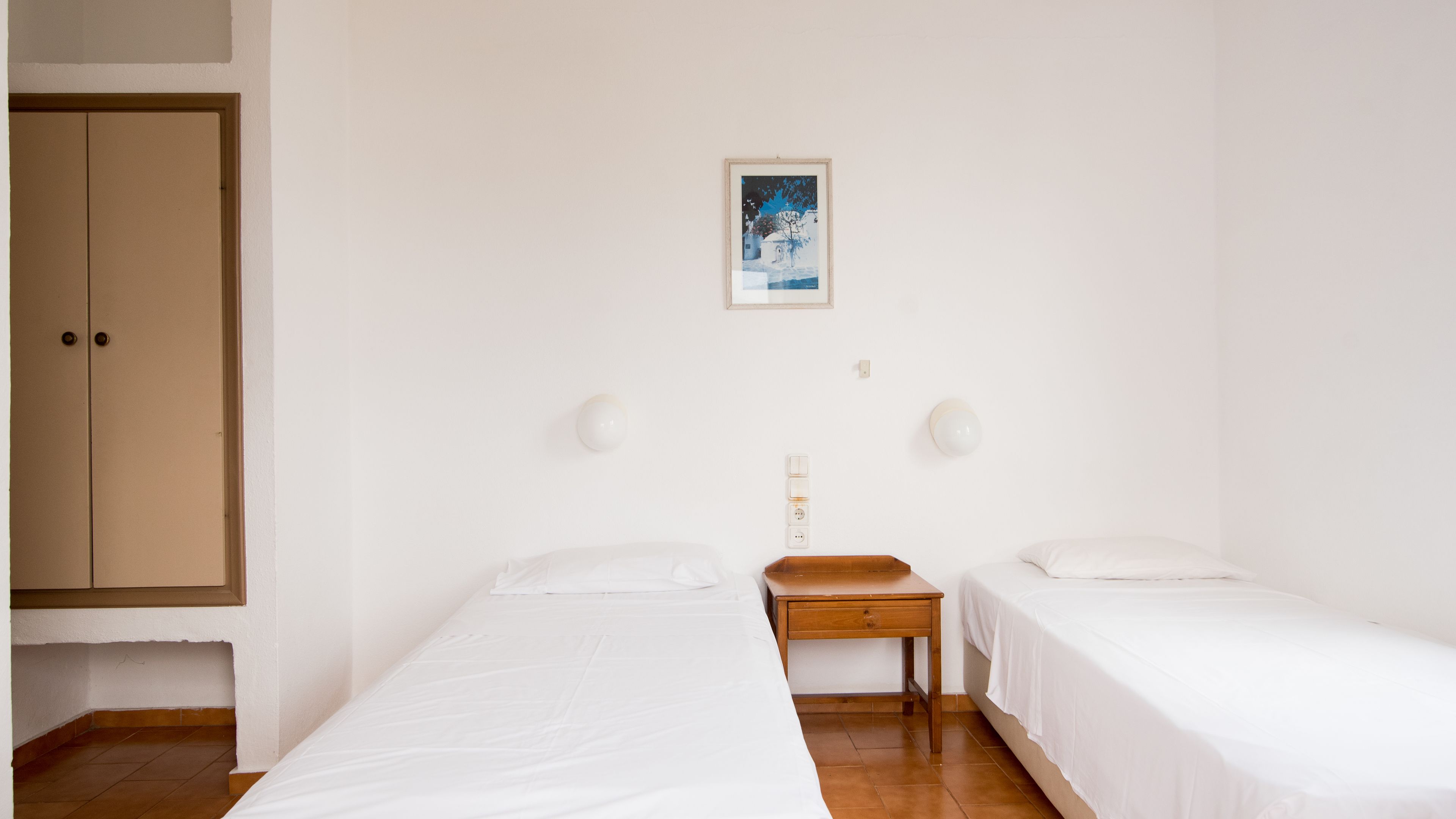 A room with two single beds, a wooden nightstand, a small table, and a wardrobe.