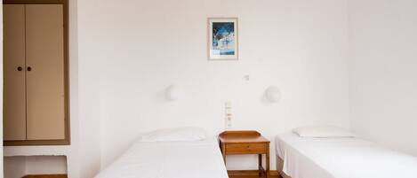 A room with two single beds, a wooden nightstand, a small table, and a wardrobe.