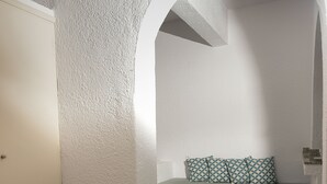 Ein Zimmer mit einer strukturierten weißen Wand, einem grünen Sofa mit gemusterten Kissen und einem weißen Tisch mit einem Getränk.