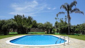 Une piscine rectangulaire bordée de pierres, entourée d’une pelouse et d’arbres.