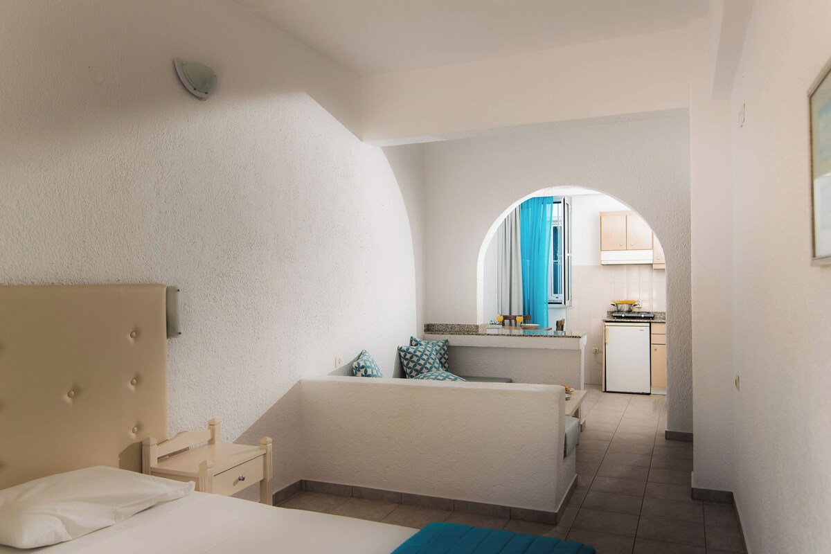 A bedroom with a bed, bedside table, and a view into the kitchen through an archway.