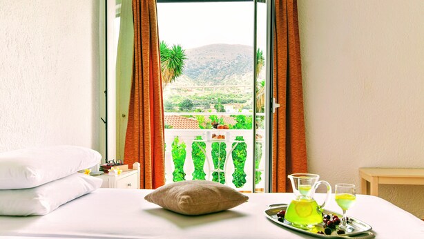 Ein Hotelzimmer mit Bett, Kissen, einem Tablett mit Getränken und Blick auf eine grüne Landschaft durch das Fenster.