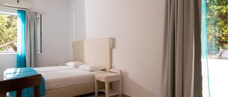 Un dormitorio con cama, mesita de noche, silla y ventana con cortinas.