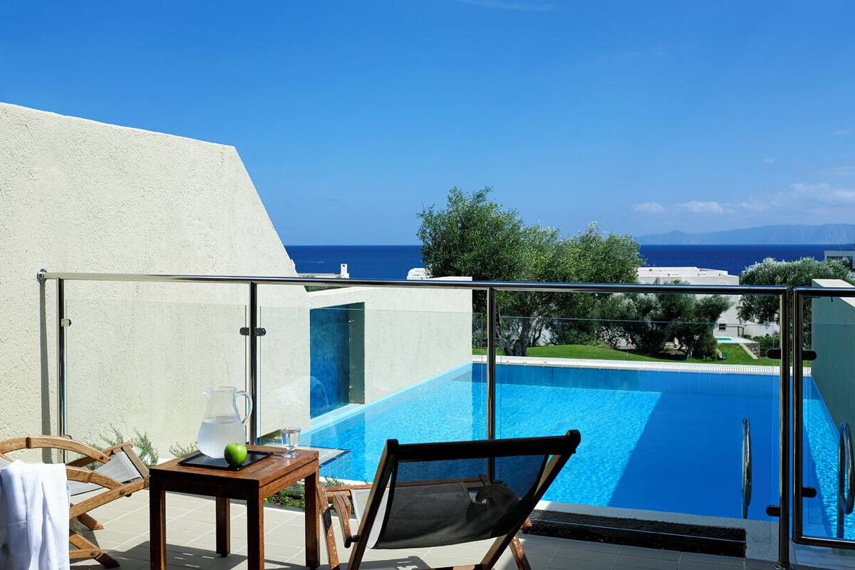 En balkon med gelænder af glas, udsigt over en swimmingpool og havet.
