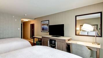 A hotel room with two beds, a desk with a flat-screen TV, a mirror, and a lamp.