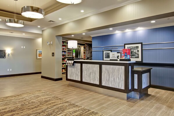 A reception area with a modern design, featuring a reception desk, a wall-mounted sign, and a well-lit interior. - Hampton Inn & Suites by Hilton Saskatoon Airport (Saskatoon)