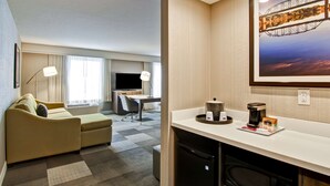 A hotel room with a sofa, desk, TV, and a painting of a bridge. - Hampton Inn & Suites by Hilton Saskatoon Airport (Saskatoon)