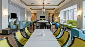 A hotel dining area with a long table, multiple chairs, and a television. - Hampton Inn & Suites by Hilton Saskatoon Airport (Saskatoon)