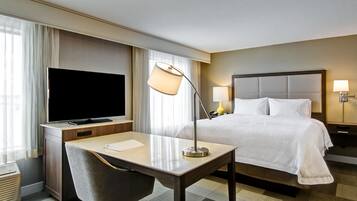 Habitación de hotel con cama, escritorio con lámpara, televisión y mesita de noche con lámpara.