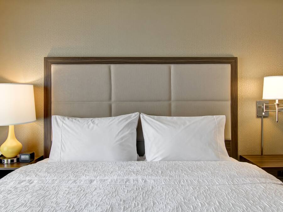 A hotel room with a large bed, two bedside lamps, a nightstand with a phone, and a wall-mounted lamp.
