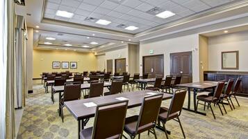 A conference room with multiple tables and chairs, a patterned carpet, and a ceiling with recessed lighting.