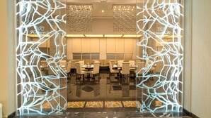 A restaurant with a modern interior, featuring a glass partition with a white abstract design, tables with chairs, and a warm lighting ambiance. - Best Western Plus Doha (Doha)