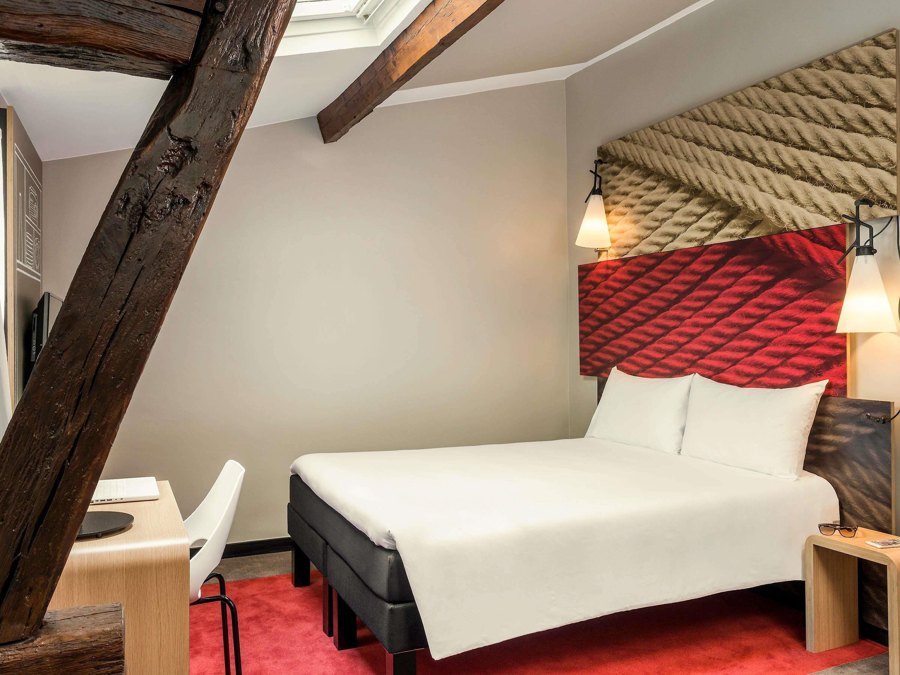 Une chambre d’hôtel comprenant un lit, un bureau, une chaise, une lampe et une tête de lit au motif texturé.