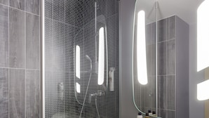Un baño moderno con ducha envuelta en vidrio, un lavabo blanco y un espejo grande.