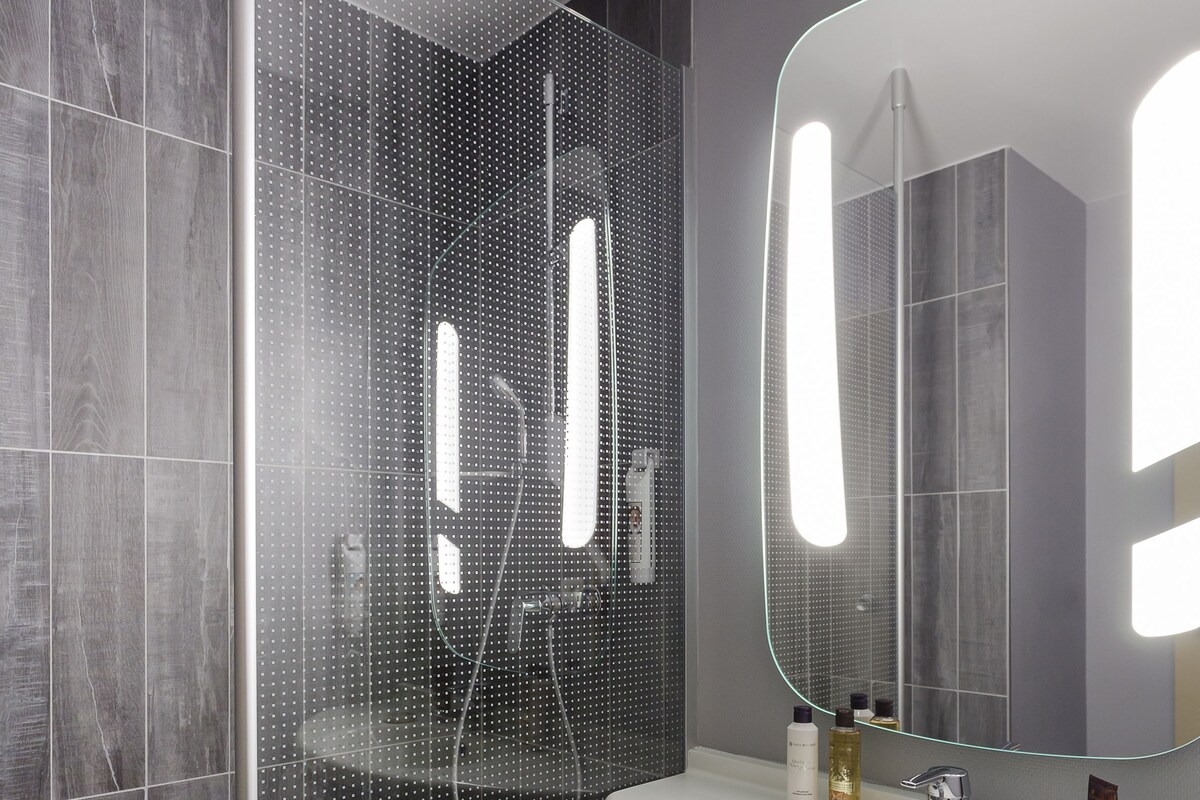 Une salle de bain moderne avec une douche à parois de verre, un lavabo blanc et un grand miroir.