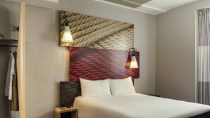 A hotel room with a bed, a small bedside table, a wardrobe, and a headboard with a patterned design. - Ibis Paris Avenue De La Republique (Paris)