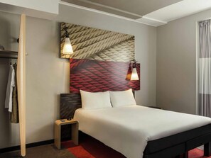 Une chambre d’hôtel comprenant un lit, une petite table de chevet, une armoire et une tête de lit ornée d’un motif décoratif.