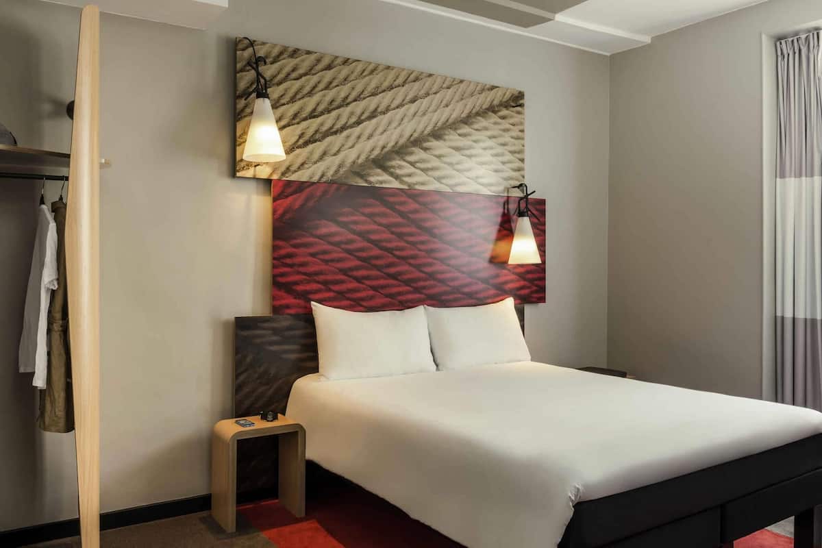 Een hotelkamer met een bed, een klein nachtkastje, een kledingkast en een hoofdeinde met een patroon.
