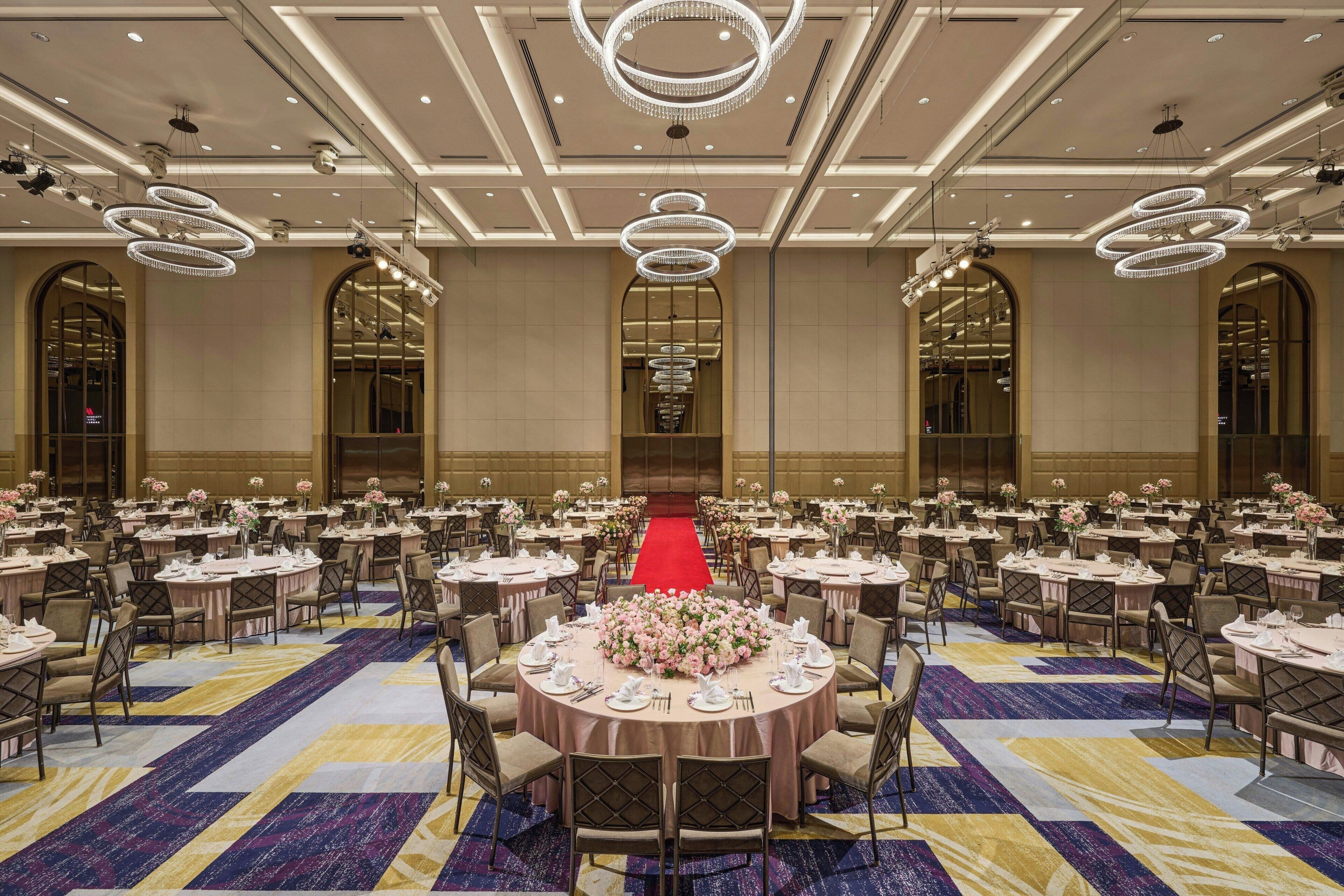 Une salle de banquet avec des tables rondes, des chaises et un tapis rouge menant à une scène.