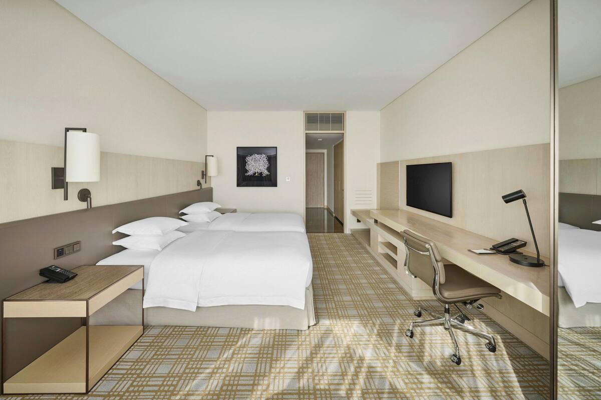 A hotel room with a bed, bedside table, desk, chair, TV, and a wall-mounted artwork.