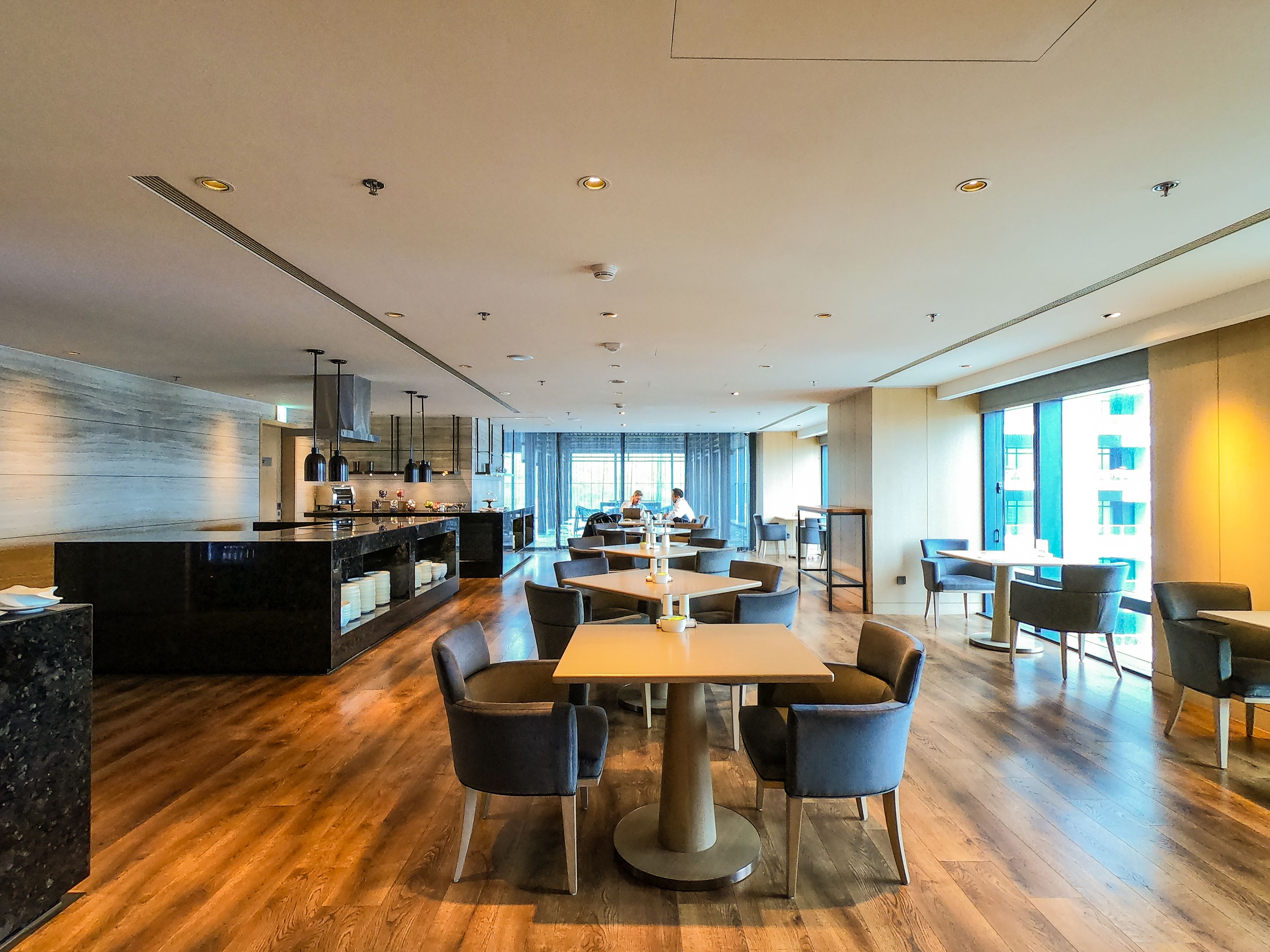Un restaurant moderne doté d’un plancher en bois, d’un comptoir de bar noir et de plusieurs tables à manger accompagnées de chaises.