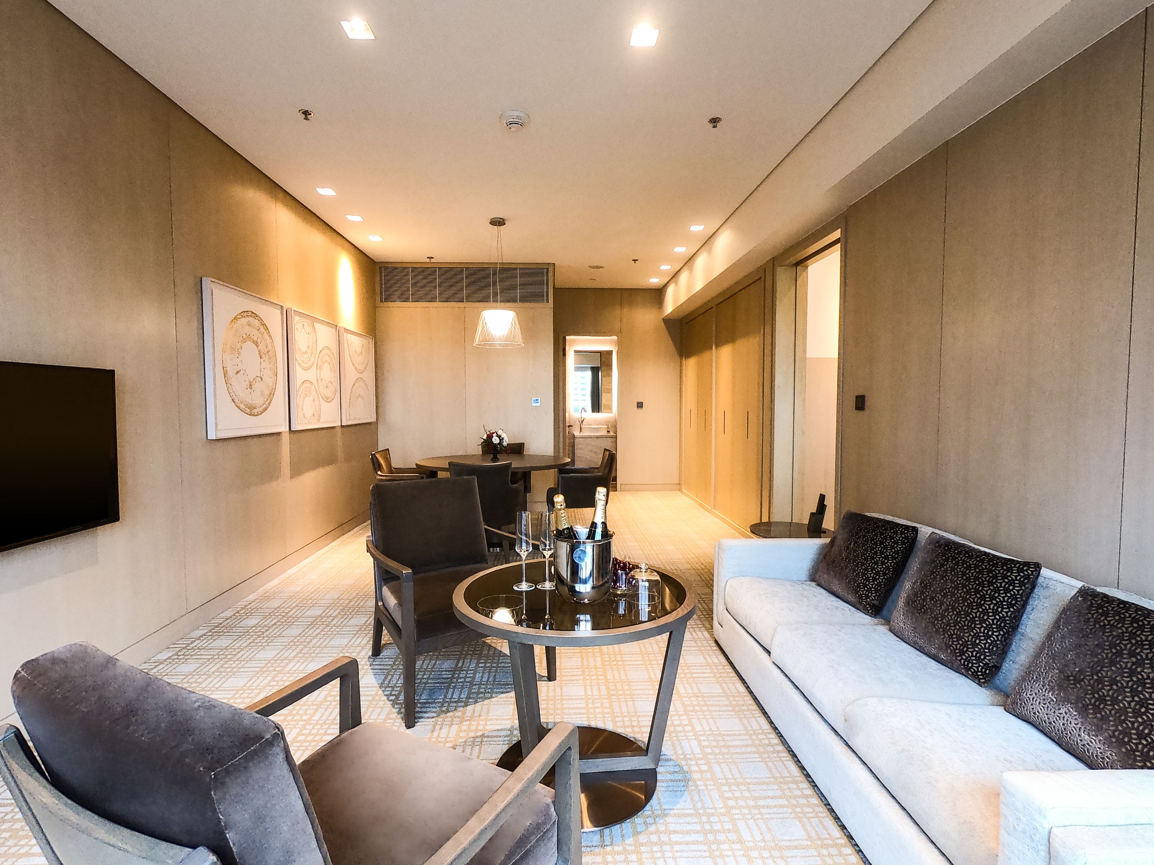 Una habitación de hotel moderna con sofá, sillas, una mesa de comedor y televisión.