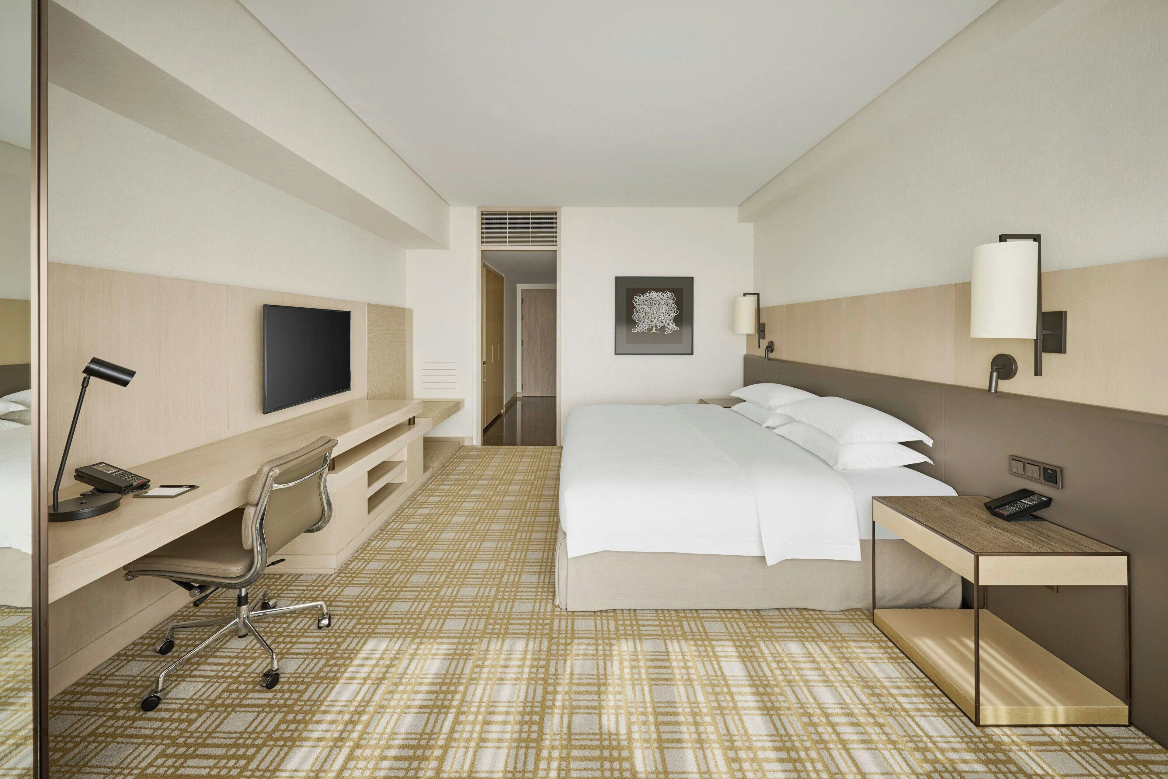 A hotel room with a bed, desk, chair, TV, and a painting on the wall.