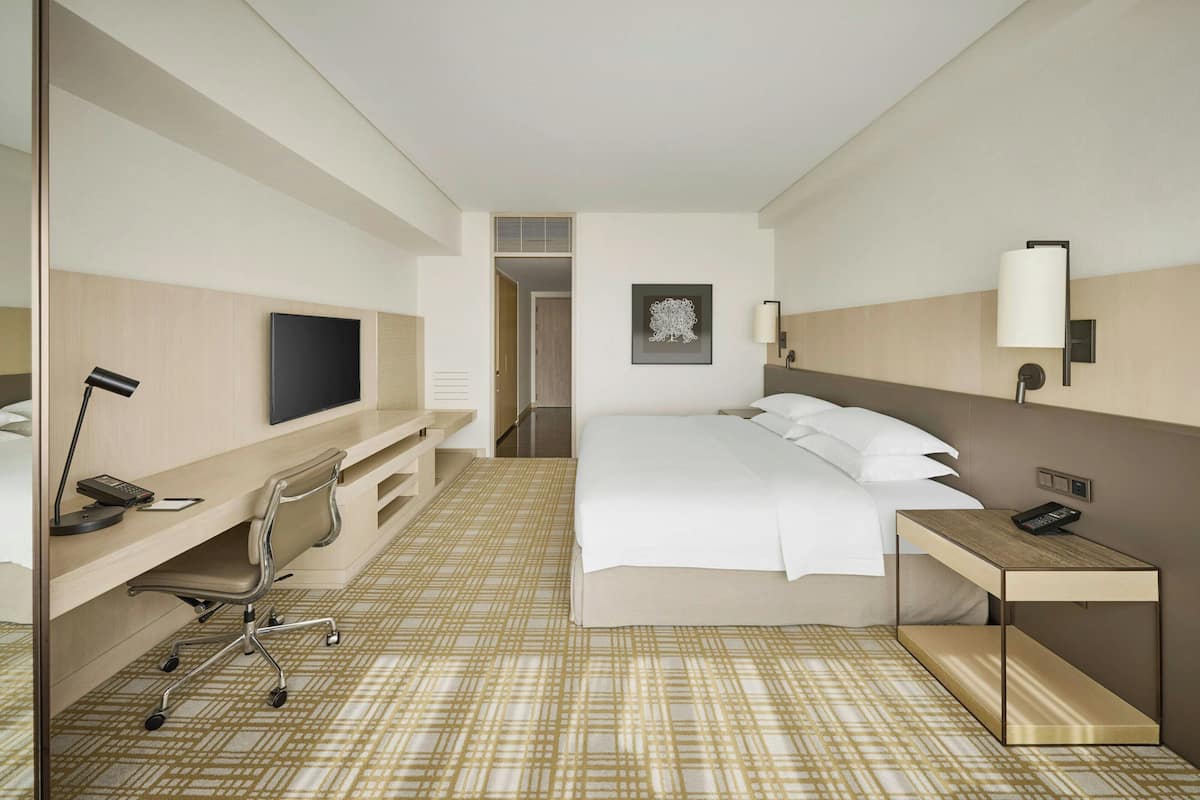 A hotel room with a bed, desk, chair, TV, and a painting on the wall.