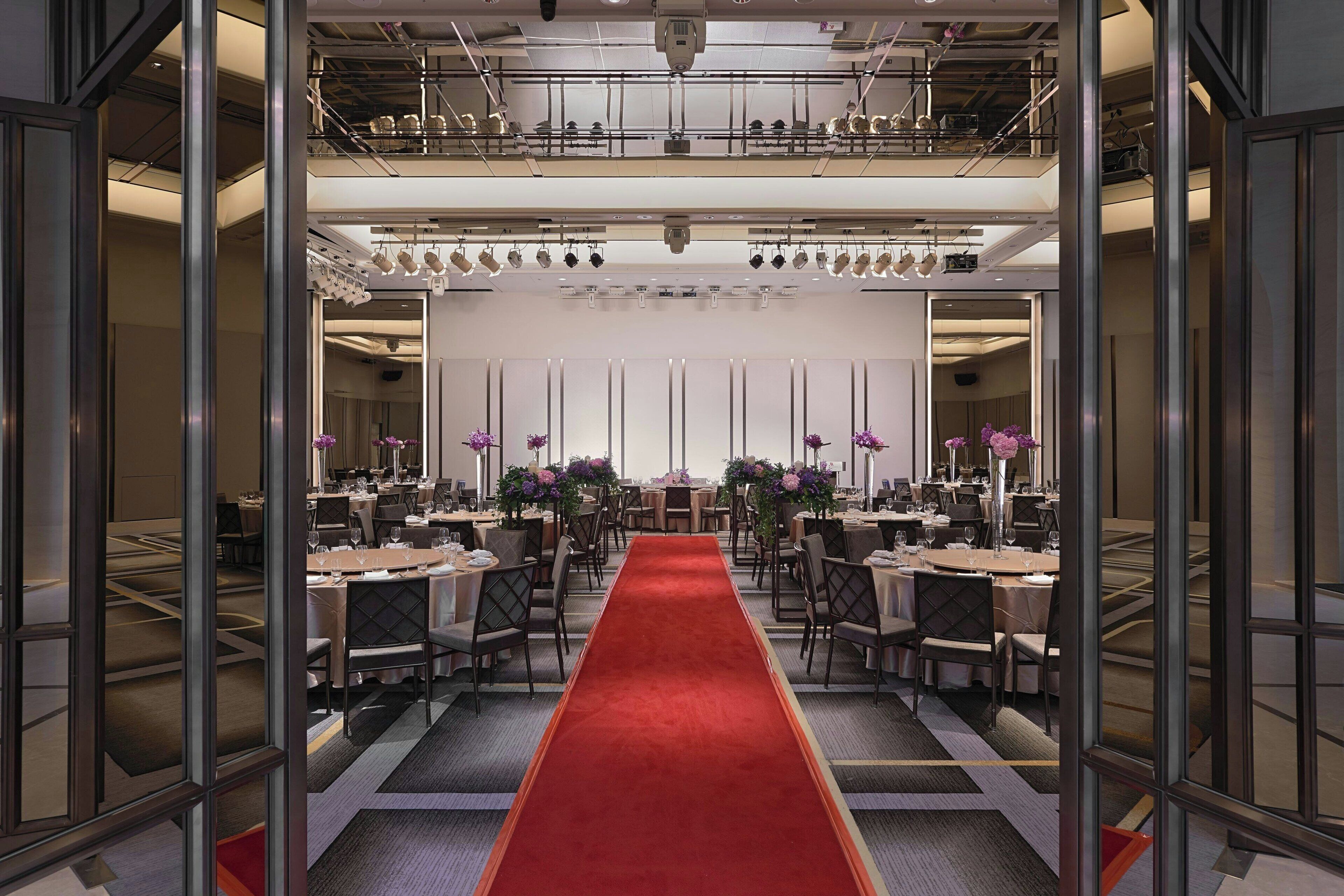 Une salle de conférence dotée d’un tapis rouge, de plusieurs tables, de chaises et d’une scène équipée d’un système d’éclairage.