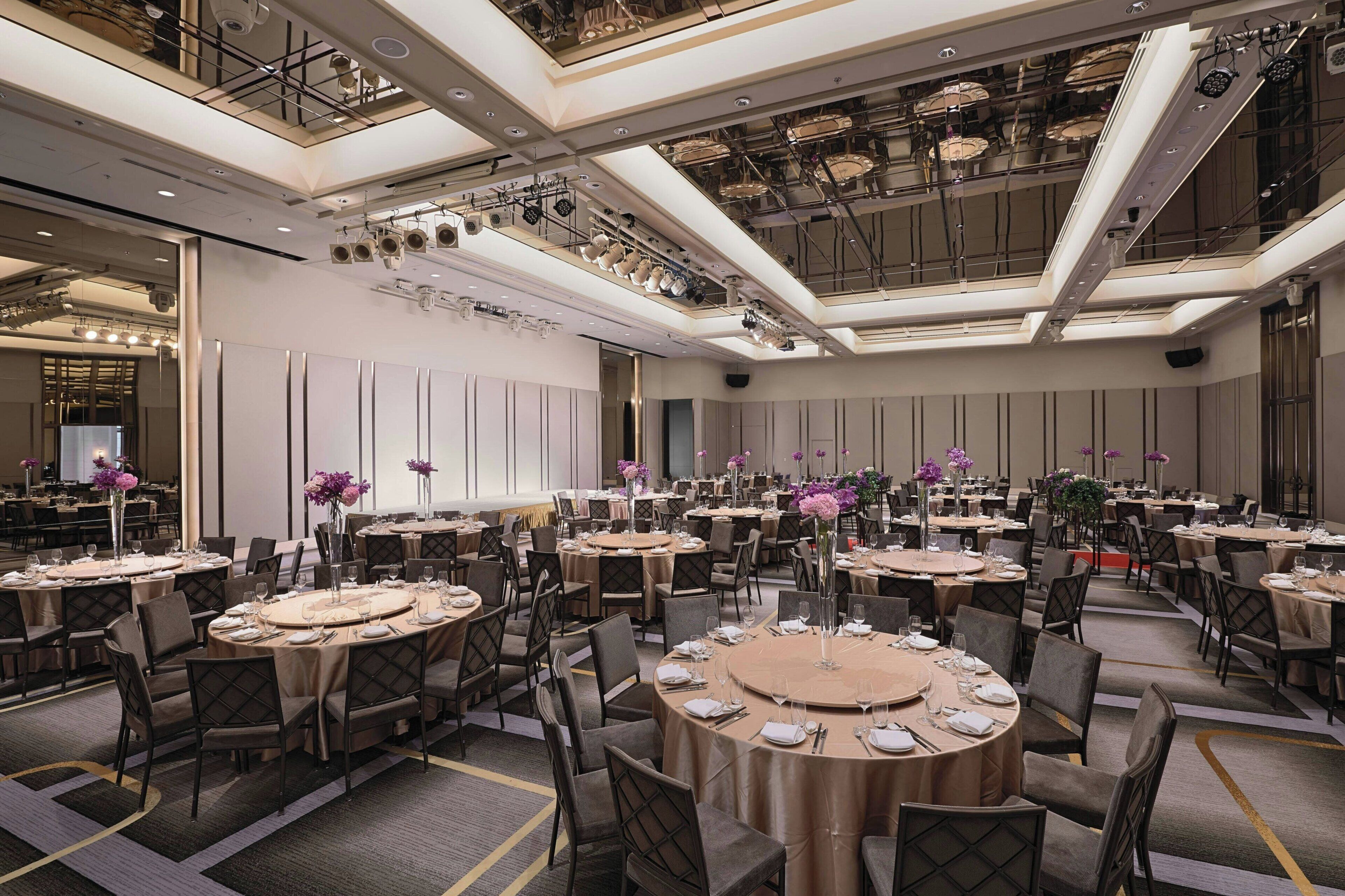 A large banquet hall with round tables, chairs, and floral centerpieces.