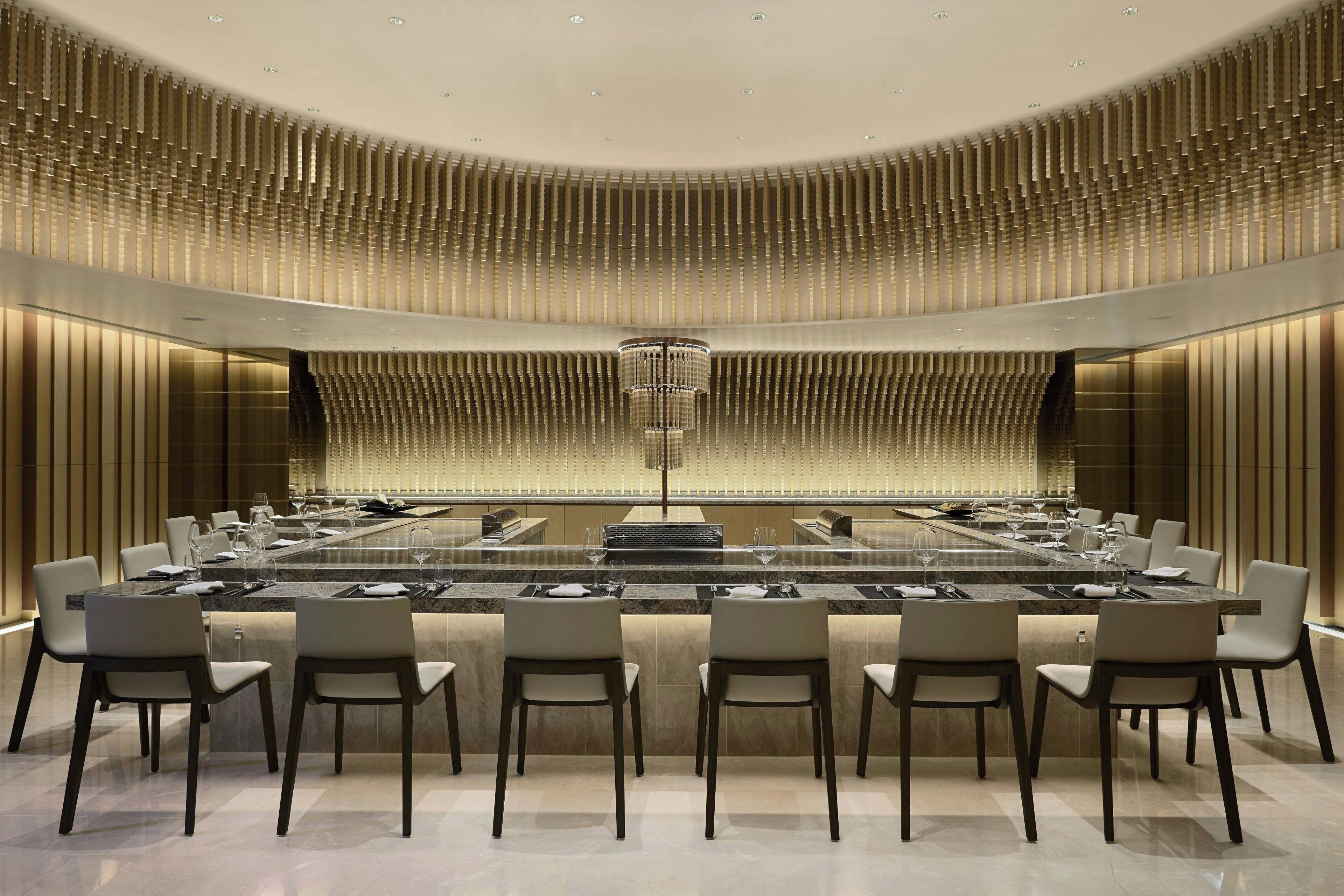 A modern dining area with a long table, multiple chairs, and a central chandelier.
